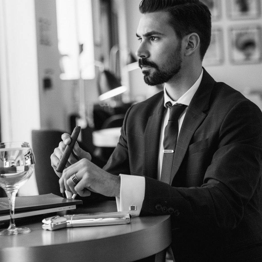 Homem elegante em traje social sentado em cafe mostrando anel masculino prata Topazio 1874 no dedo.